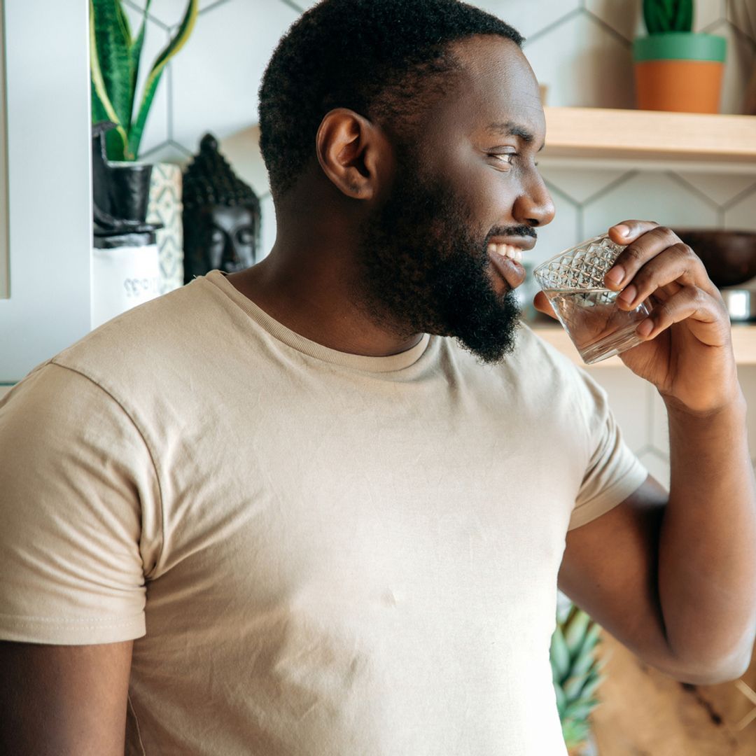 A man smiling while holding a glass of water in a kitchen.