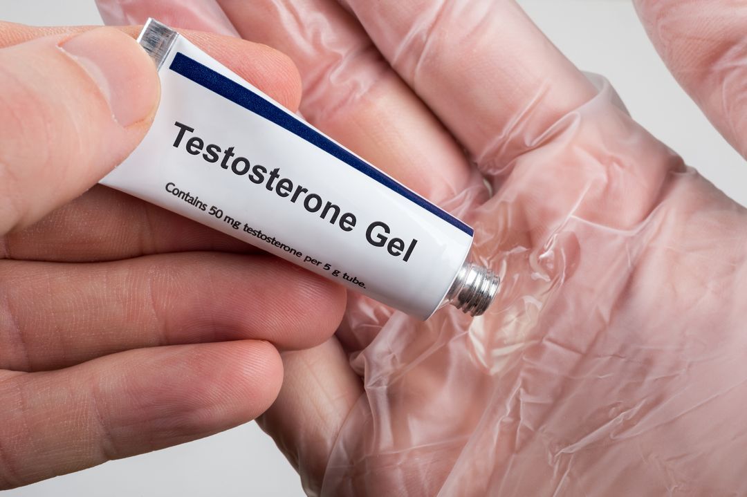 Hand holding testosterone gel against hand in glove. 
